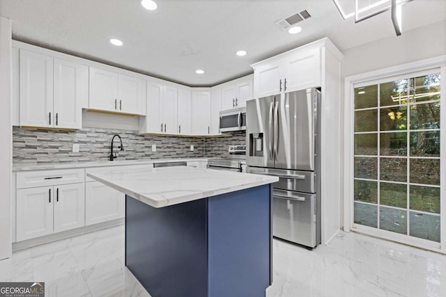 kitchen featuring light stone counters, stainless steel appliances, sink, a center island, and white cabinetry