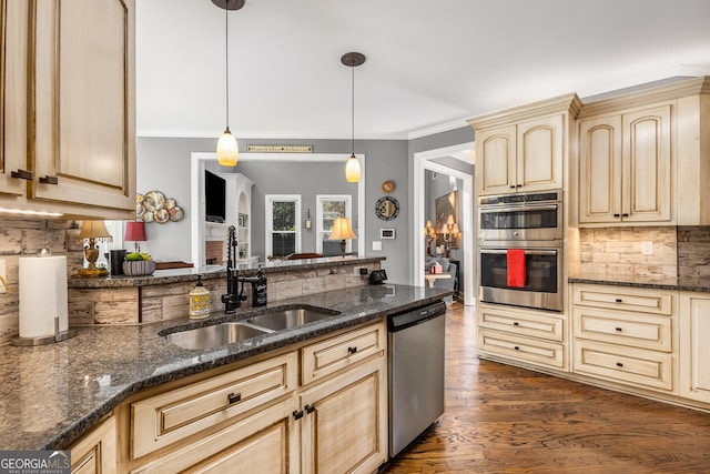 kitchen featuring appliances with stainless steel finishes, light brown cabinetry, dark stone counters, sink, and decorative light fixtures