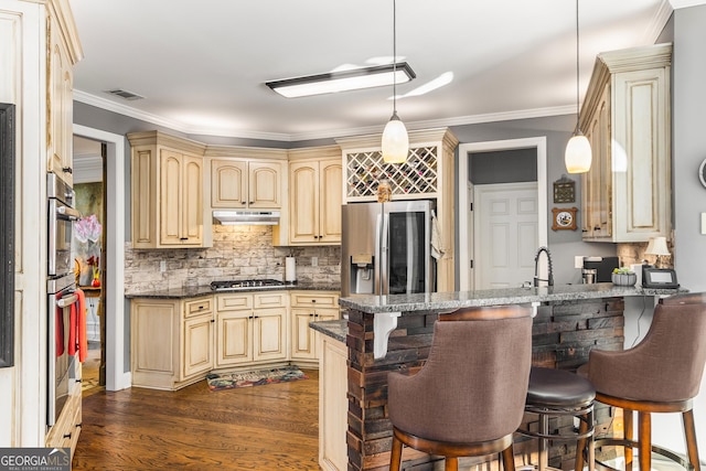 kitchen with a kitchen bar, appliances with stainless steel finishes, kitchen peninsula, dark stone counters, and decorative light fixtures