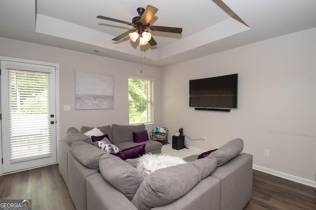 living room featuring ceiling fan, a raised ceiling, and dark wood-type flooring