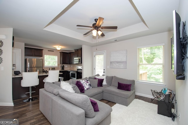 living room featuring dark hardwood / wood-style flooring, a tray ceiling, and ceiling fan