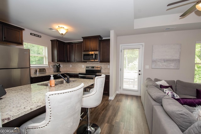 kitchen with a breakfast bar, a kitchen island with sink, sink, dark brown cabinets, and stainless steel appliances