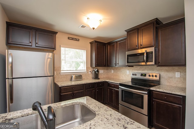 kitchen with tasteful backsplash, light stone counters, dark brown cabinets, stainless steel appliances, and sink