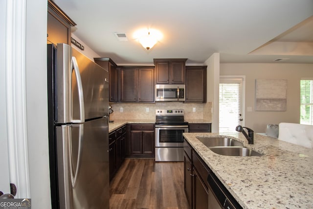 kitchen featuring appliances with stainless steel finishes, backsplash, light stone counters, dark wood-type flooring, and sink