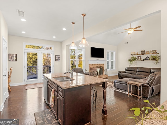 kitchen featuring pendant lighting, sink, an island with sink, dark brown cabinets, and light stone counters