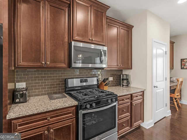 kitchen with backsplash, light stone countertops, stainless steel appliances, and dark hardwood / wood-style floors