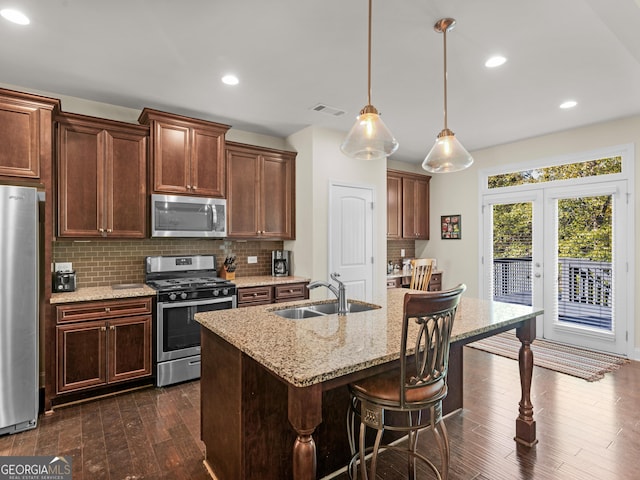 kitchen with backsplash, a center island with sink, sink, hanging light fixtures, and stainless steel appliances