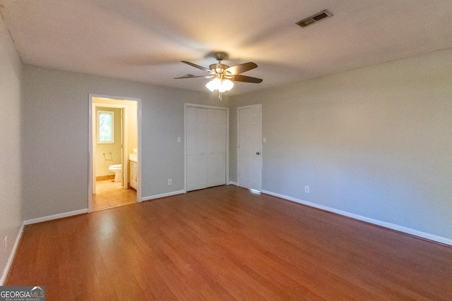 unfurnished bedroom with wood-type flooring, ensuite bath, ceiling fan, and a closet