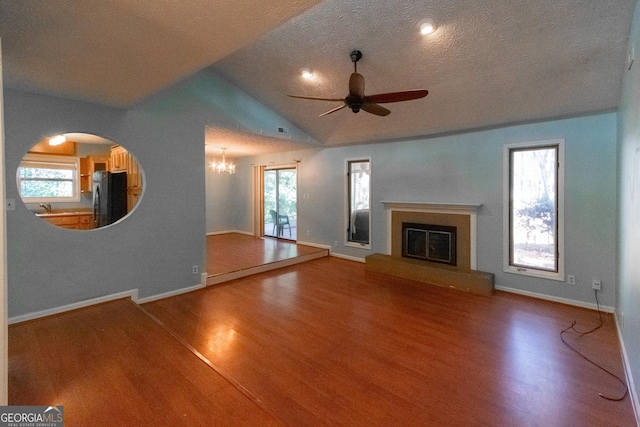 unfurnished living room featuring ceiling fan with notable chandelier, vaulted ceiling, a textured ceiling, and wood-type flooring