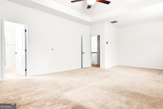 spare room featuring a raised ceiling, ceiling fan, crown molding, and light carpet