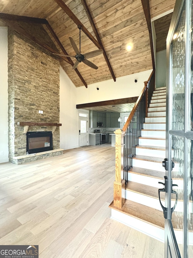 interior space with ceiling fan, wooden ceiling, a stone fireplace, high vaulted ceiling, and light wood-type flooring