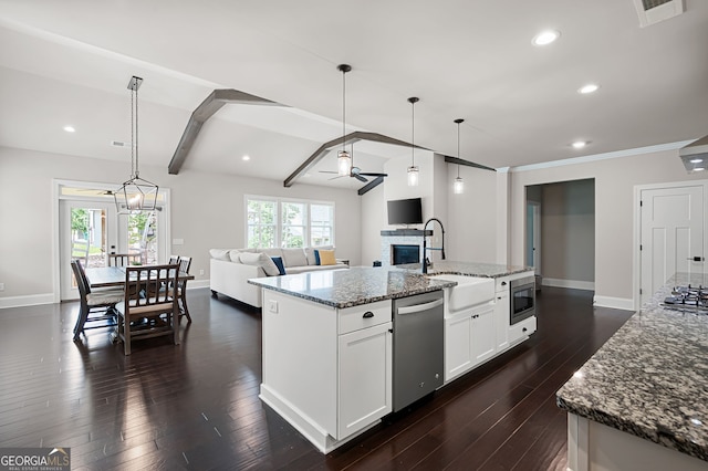 kitchen featuring light stone countertops, stainless steel appliances, a kitchen island with sink, decorative light fixtures, and white cabinetry