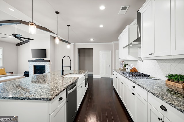 kitchen featuring hanging light fixtures, a stone fireplace, a large island with sink, dark stone counters, and white cabinets