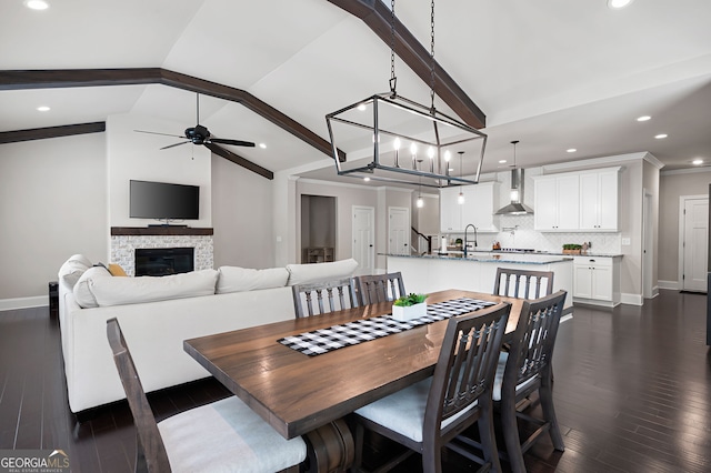 dining area with lofted ceiling with beams, dark hardwood / wood-style flooring, a fireplace, and ceiling fan with notable chandelier