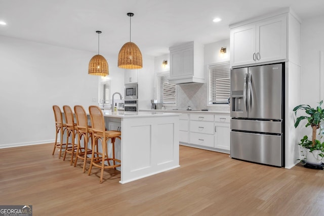 kitchen with backsplash, stainless steel appliances, pendant lighting, a center island with sink, and white cabinetry