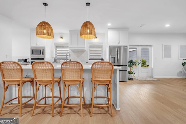 kitchen featuring hanging light fixtures, white cabinets, stainless steel appliances, and light hardwood / wood-style floors