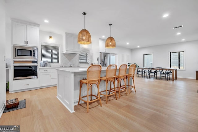 kitchen featuring white cabinetry, a kitchen island, decorative light fixtures, and appliances with stainless steel finishes