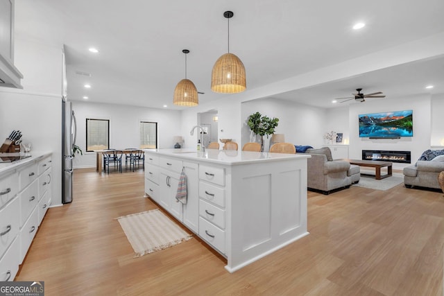 kitchen featuring white cabinetry, ceiling fan, stainless steel fridge, decorative light fixtures, and a center island with sink