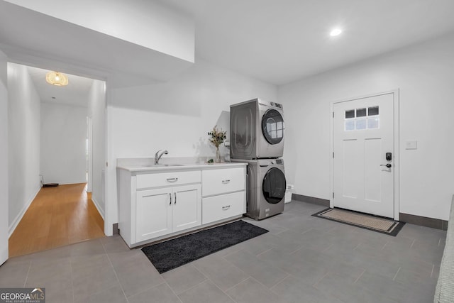 washroom featuring light tile patterned flooring, cabinets, stacked washing maching and dryer, and sink