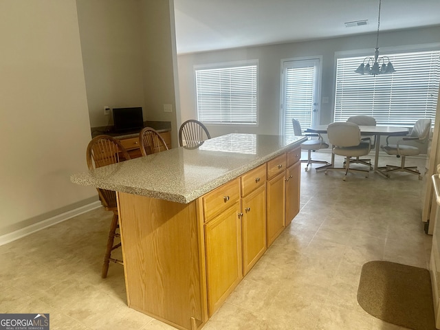 kitchen with visible vents, decorative light fixtures, a kitchen breakfast bar, a kitchen island, and light stone countertops