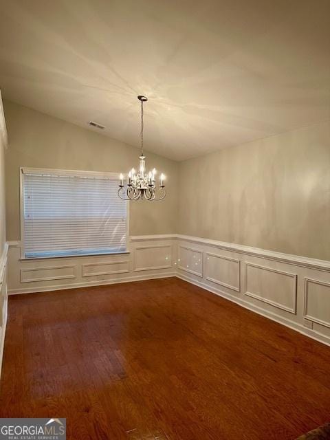 unfurnished dining area with a wainscoted wall, visible vents, an inviting chandelier, lofted ceiling, and dark wood-style flooring