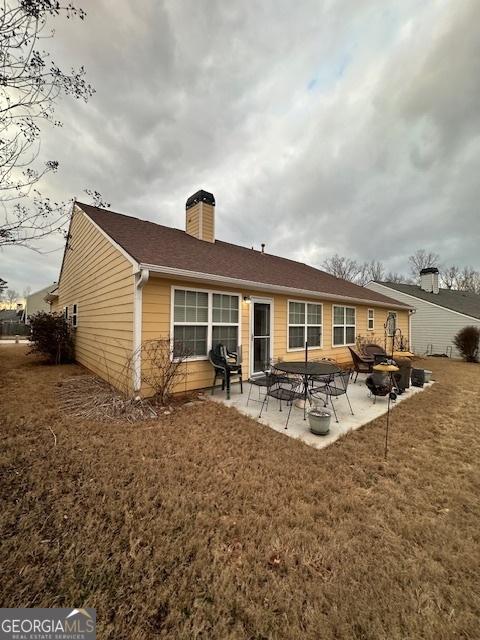 rear view of property featuring a patio area, a lawn, and a chimney