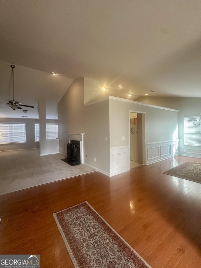 unfurnished living room featuring wood finished floors, a fireplace, ceiling fan, vaulted ceiling, and a decorative wall