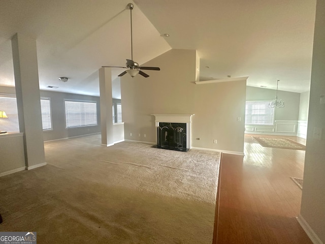 unfurnished living room featuring a fireplace with flush hearth, lofted ceiling, ceiling fan with notable chandelier, carpet, and baseboards