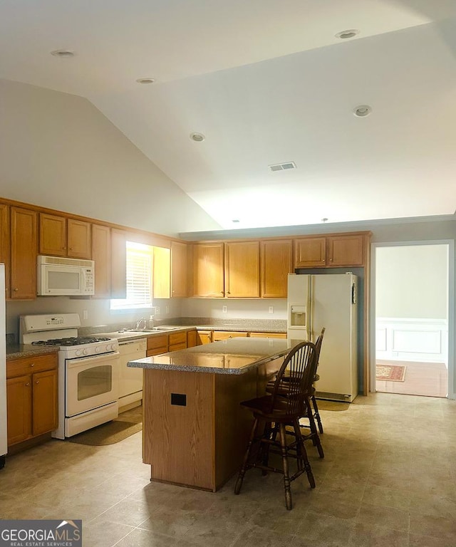 kitchen featuring visible vents, a sink, a center island, white appliances, and a breakfast bar area