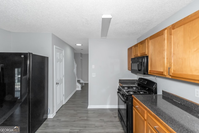 kitchen with black appliances, dark wood-type flooring, dark stone counters, and a textured ceiling