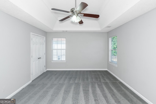 spare room with a raised ceiling, a wealth of natural light, ceiling fan, and dark carpet