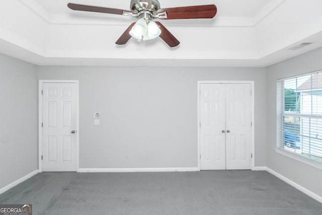 empty room with dark carpet, a raised ceiling, and ceiling fan