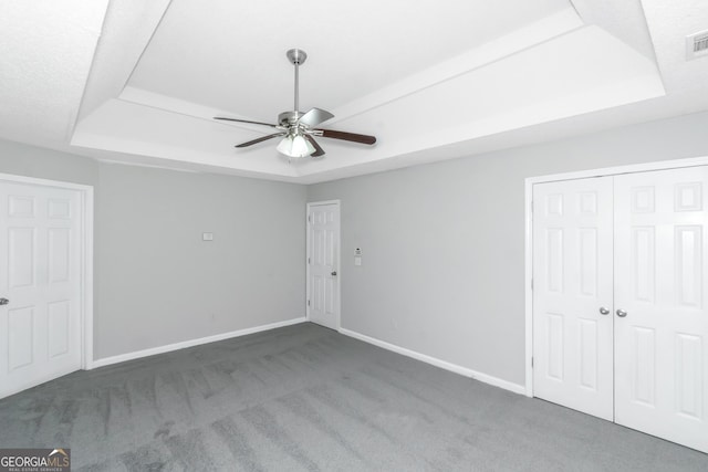 unfurnished bedroom with a tray ceiling, ceiling fan, and dark carpet