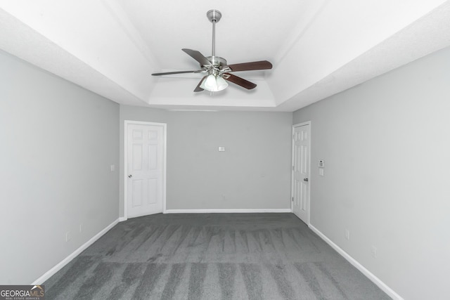 unfurnished room with dark colored carpet, ceiling fan, and a tray ceiling