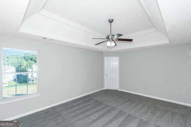 spare room featuring dark colored carpet, a raised ceiling, and ceiling fan