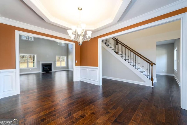 unfurnished living room featuring wood-type flooring, stairway, a raised ceiling, a wainscoted wall, and a chandelier