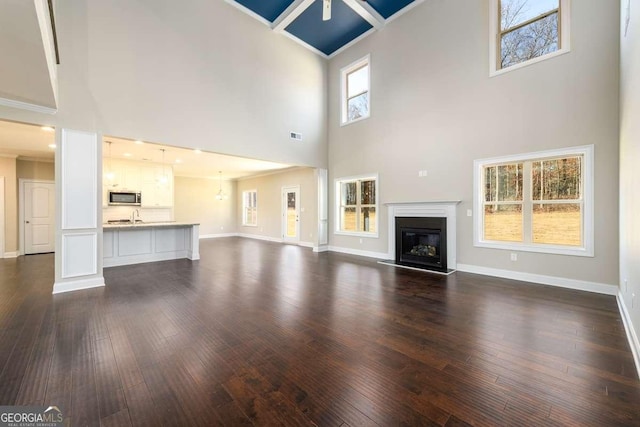 unfurnished living room with a glass covered fireplace, baseboards, dark wood-style floors, and a towering ceiling