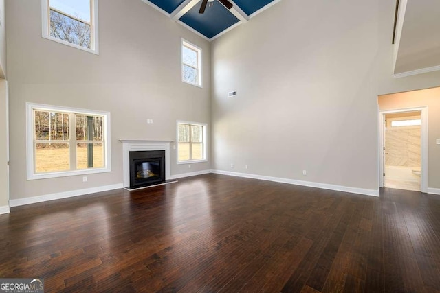unfurnished living room featuring a ceiling fan, dark wood-style flooring, baseboards, a glass covered fireplace, and a high ceiling