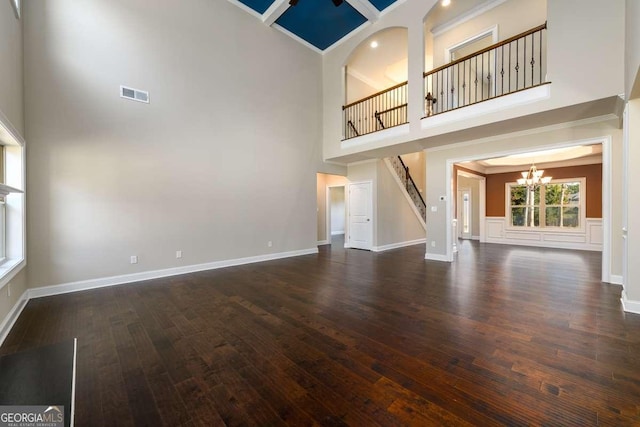 unfurnished living room with wood finished floors, visible vents, an inviting chandelier, a towering ceiling, and crown molding