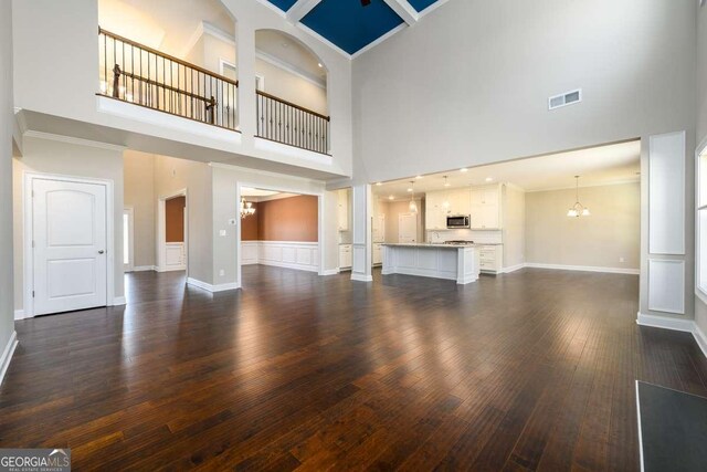 unfurnished living room featuring visible vents, dark wood-type flooring, a high ceiling, and a notable chandelier