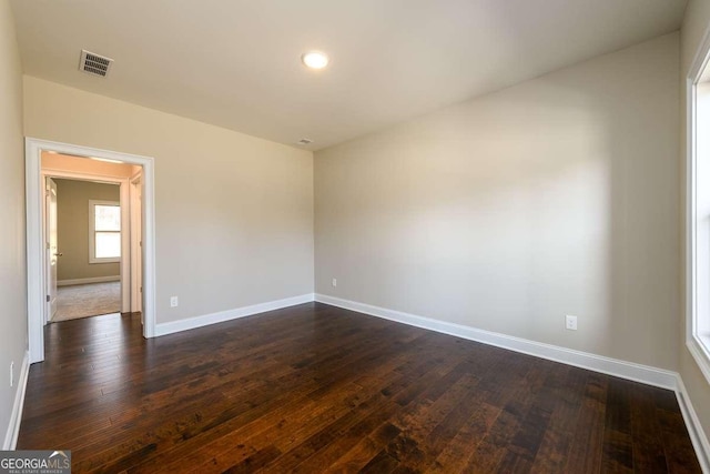 unfurnished room featuring baseboards, dark wood finished floors, and visible vents