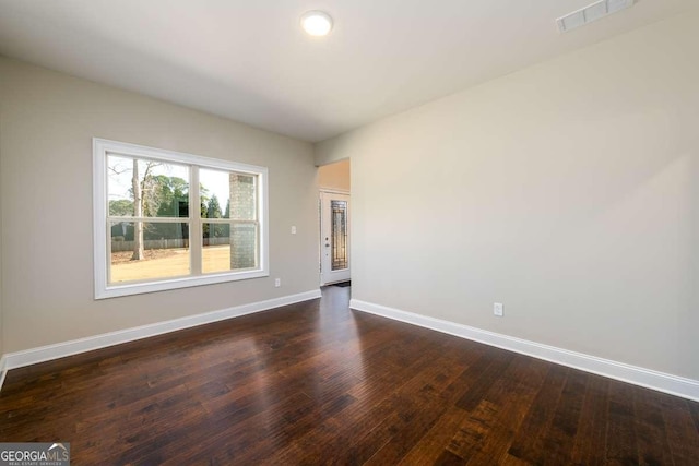 unfurnished room with baseboards, visible vents, and dark wood-style flooring