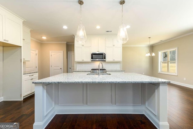 kitchen with decorative backsplash, a sink, white cabinets, stainless steel microwave, and dark wood-type flooring