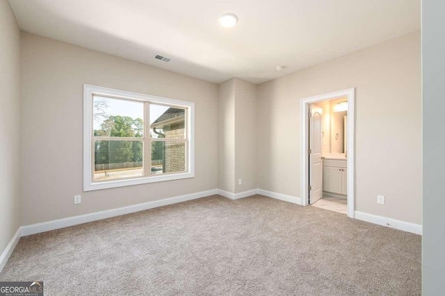 unfurnished bedroom featuring light colored carpet, baseboards, ensuite bath, and visible vents