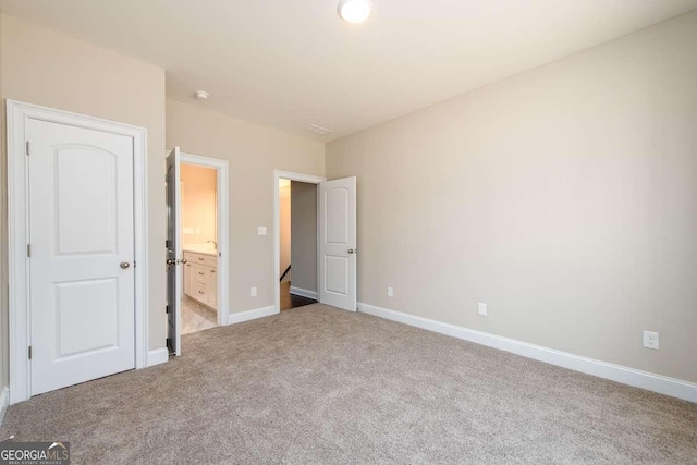 unfurnished bedroom featuring baseboards, light carpet, and ensuite bathroom