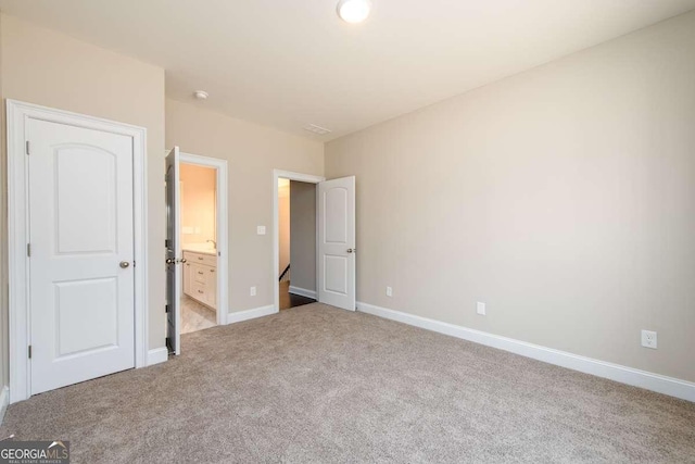 unfurnished bedroom with baseboards, light carpet, and ensuite bath