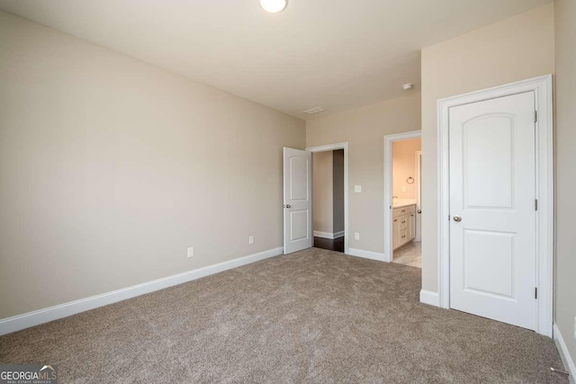 unfurnished bedroom with baseboards, light colored carpet, and ensuite bath