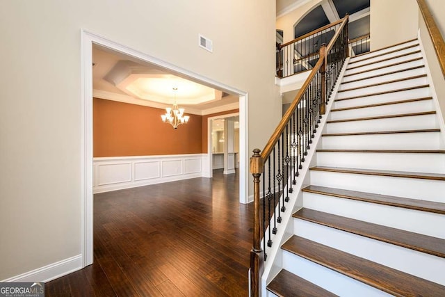 stairs with an inviting chandelier, a tray ceiling, visible vents, ornamental molding, and hardwood / wood-style flooring