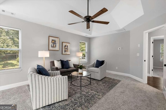 carpeted living room featuring a raised ceiling and ceiling fan