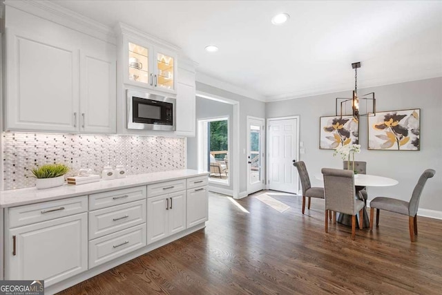 kitchen featuring light stone countertops, backsplash, built in microwave, white cabinets, and hanging light fixtures